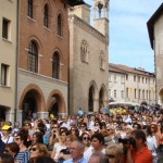 Hundreds of readers sit in a nice piazza to listen to an author present his book.